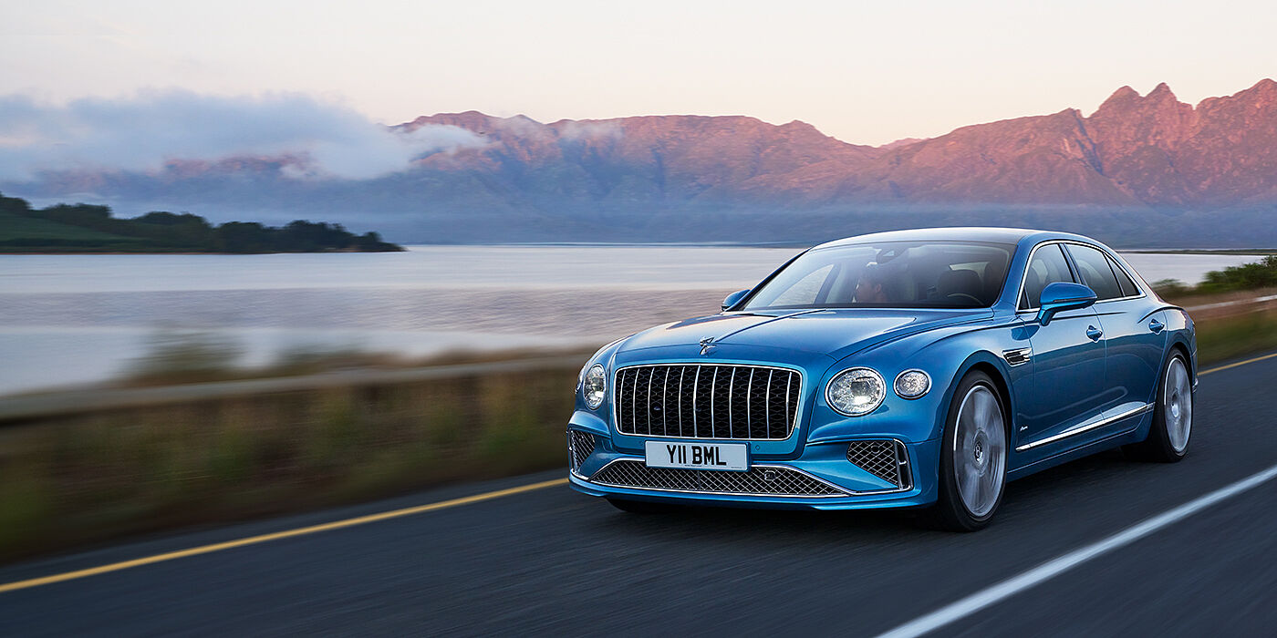 Bentley Cairo New Bentley Flying Spur Azure sedan in Light windsor blue paint by Mulliner, with 22 inch Azure wheels and chrome straight vaned grille driving on a mountain road