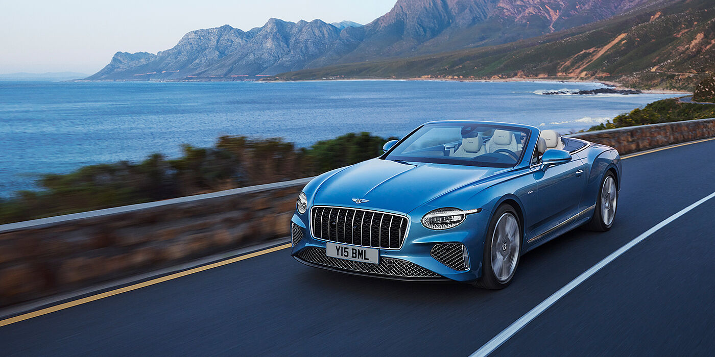 Bentley Cairo New Bentley Continental GTC Azure convertible in Light Windsor blue paint with 22 inch Azure wheels and chrome grill, driving dynamically by the sea