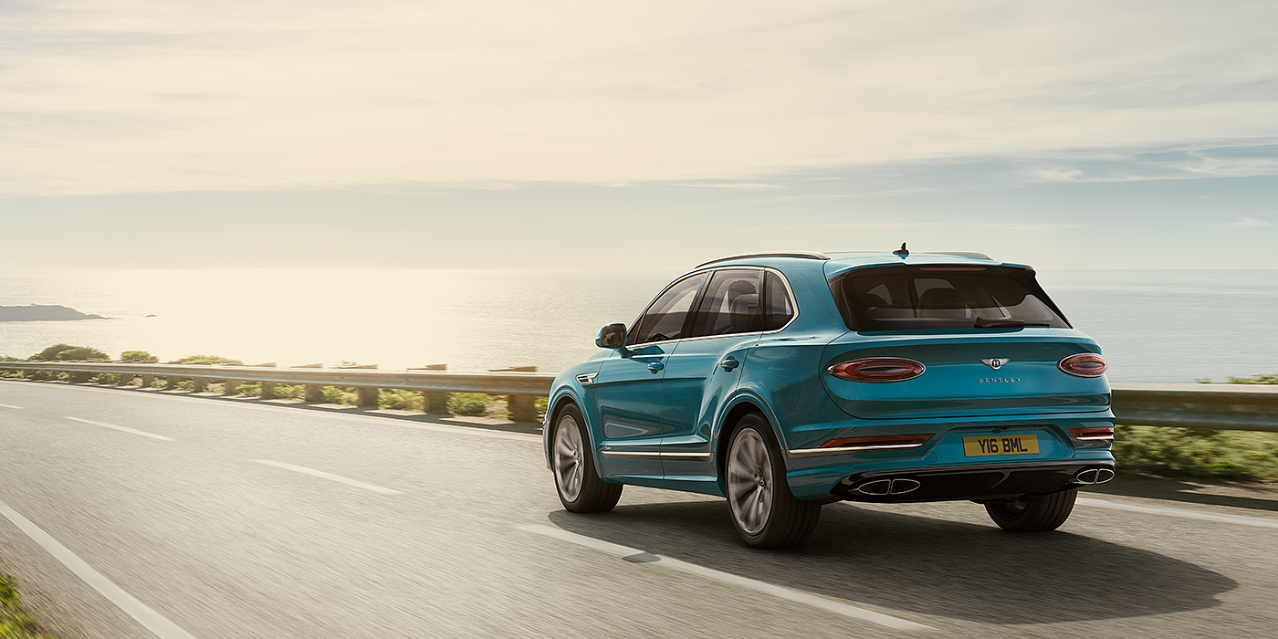 Bentley Cairo Bentley Bentayga Azure luxury SUV rear three quarter in Topaz Blue by Mulliner paint, driving on an ocean road.
