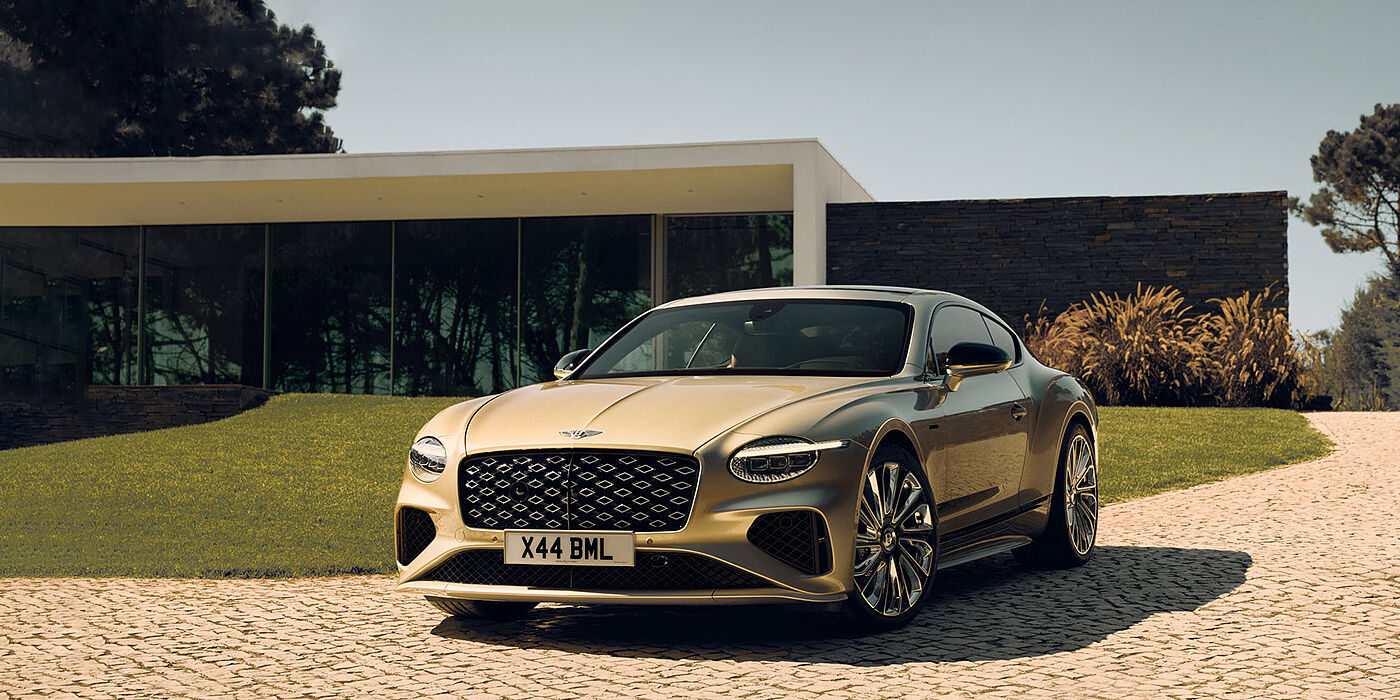 Bentley Cairo Bentley Continental GT Mulliner coupe front three quarters in Patina paint parked outside a glass fronted building with a grass lawn behind it