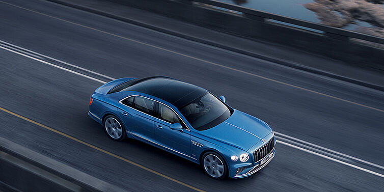 Bentley Cairo New Bentley Flying Spur Azure sedan in Light windsor blue paint by Mulliner, with 22 inch Azure wheels seen from overhead driving dynamically on a country road
