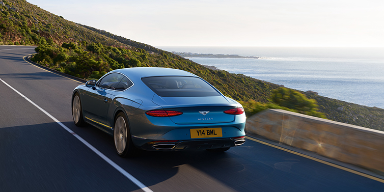 Bentley Cairo New Bentley Continental GT Azure coupe in Light Windsor blue paint seen from the rear driving dynamically on a seaside road